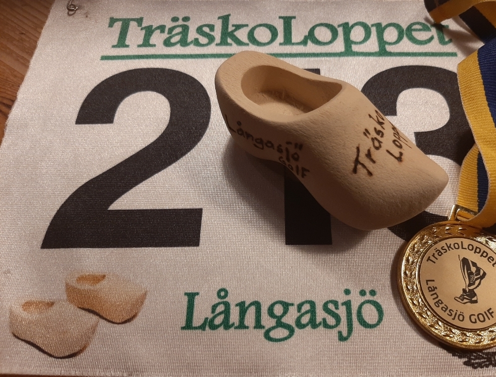 Nummerlapp med TräskoLoppets gröna logotyp, en liten träsko i trä och en guldmedalj med gulblått band.