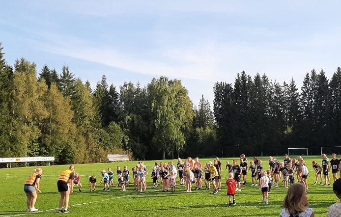 Deltagare i alla åldrar värmer upp tillsammans på gräsplanen vid Långasjö Idrottsplats en solig septemberkväll.